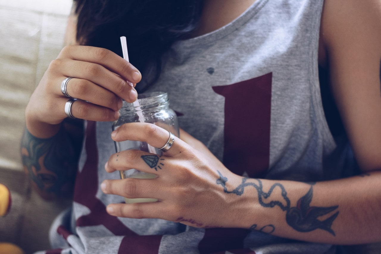 A woman wearing sterling silver rings sips a drink out of a mason jar. A woman wearing sterling silver rings sips a drink out of a mason jar.