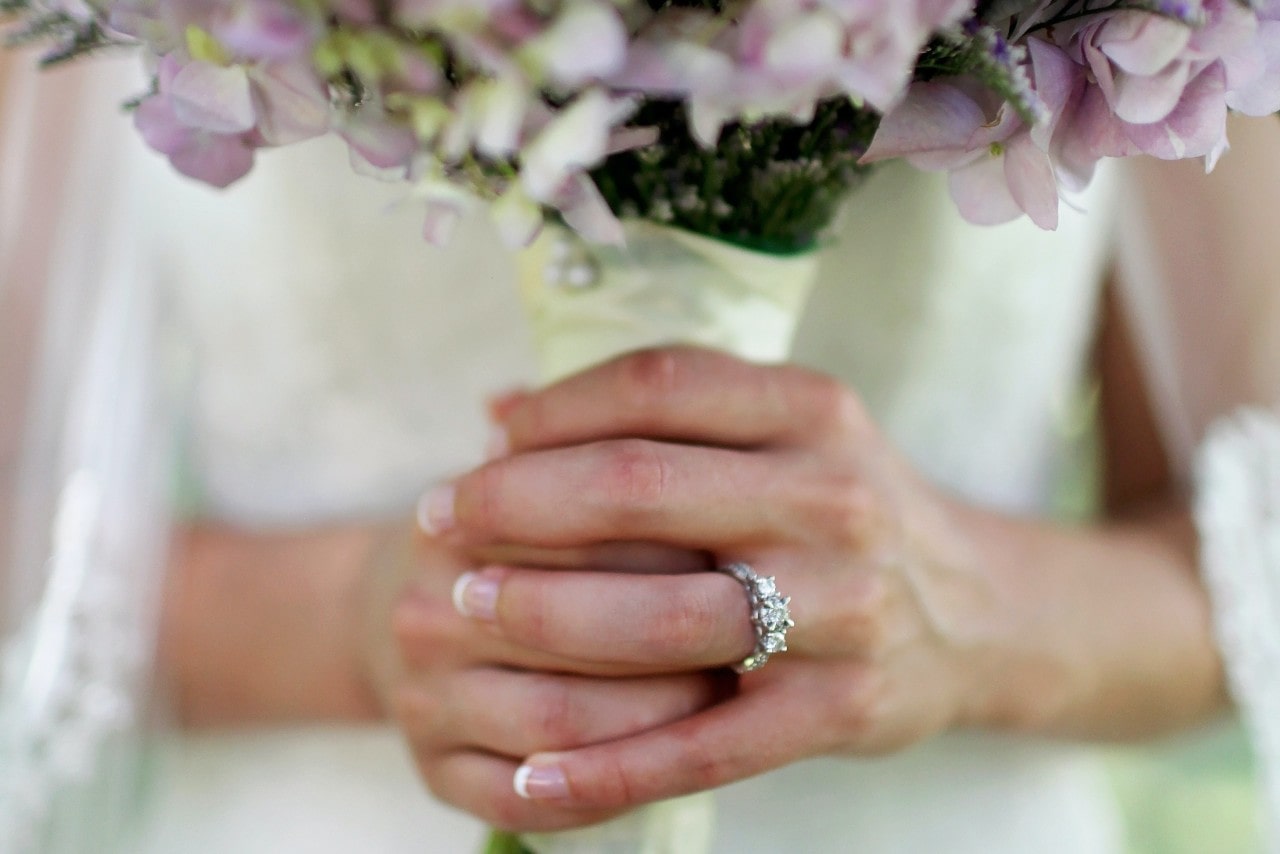 Close up image of a bride's hands holding a bouquet of flowers, wearing a three stone diamond engagement ring Close up image of a bride's hands holding a bouquet of flowers, wearing a three stone diamond engagement ring