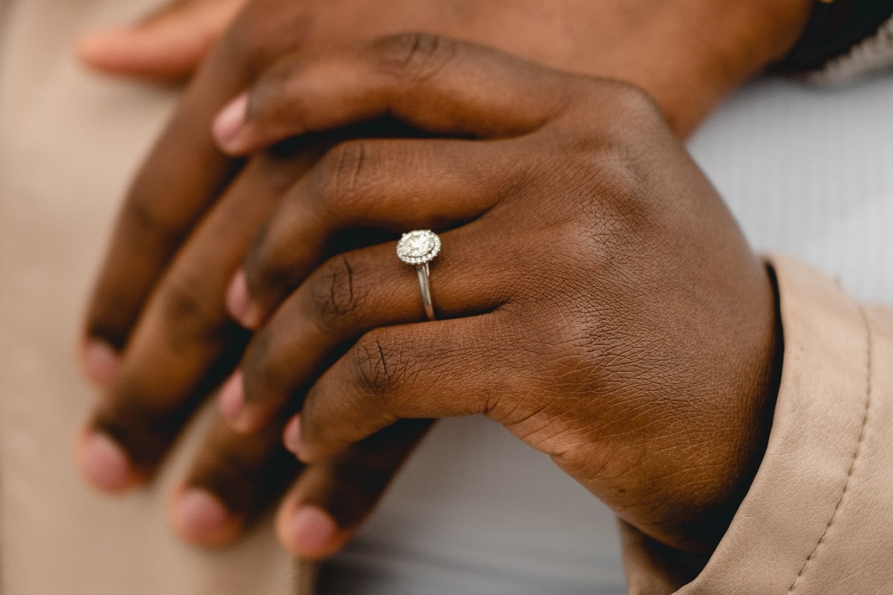 Two hands holding, one of them wearing a silver, oval cut, diamond engagement ring Two hands holding, one of them wearing a silver, oval cut, diamond engagement ring